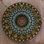 A circular LED mandala wall light with intricate layered cutouts in blue, green, orange, and white, featuring an Om symbol in the center, shown lit against a wooden background. image 3