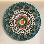 A circular mandala wall hanging with intricate layered geometric and floral patterns in teal, blue, orange, and white, mounted on a textured beige wall. image 7