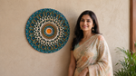 A woman in a beige floral saree stands next to a large, circular, hand-woven mandala wall hanging in teal, gold, and cream colors, mounted on a textured beige wall. image 11