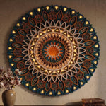 A large circular wooden mandala wall art piece with intricate carved floral and geometric patterns, illuminated by warm internal lights, mounted on a textured beige wall with a vase of flowers and books at the bottom. image 8
