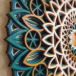 Close-up of a multicolor wooden mandala wall art piece with layered geometric and floral cutout patterns in teal, blue, orange, and white, mounted on a beige wall. image 6